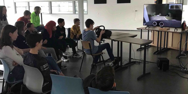 Jongen sturend in de simulator terwijl de rest van de klas kijkt.
