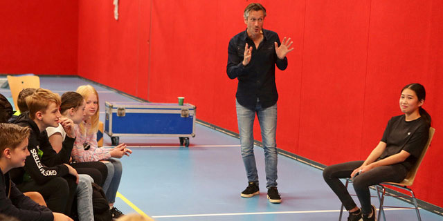 Acteur en leerling op podium terwijl leerlingen daar naar kijken