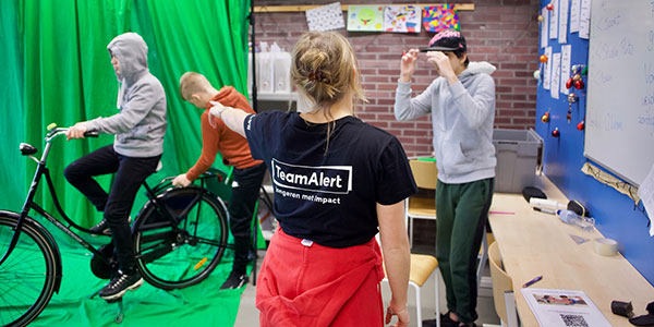 Jongen in gesprek met medewerker van Team Alert die wijst naar een andere jongen op een fiets op een groot groen doek.